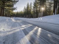 a road is covered in snow near a pine tree filled hill with trees and some snow