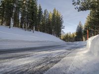 a road is covered in snow near a pine tree filled hill with trees and some snow