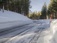 a road is covered in snow near a pine tree filled hill with trees and some snow