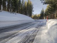 a road is covered in snow near a pine tree filled hill with trees and some snow