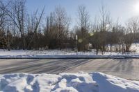 a road is covered in white snow in the middle of a wooded area with tall trees