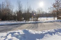 a road is covered in white snow in the middle of a wooded area with tall trees