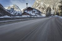 snow on the road and small buildings in the mountains side by side along a path with light poles