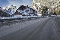 snow on the road and small buildings in the mountains side by side along a path with light poles