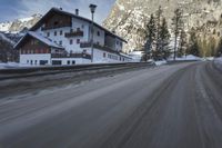 snow on the road and small buildings in the mountains side by side along a path with light poles