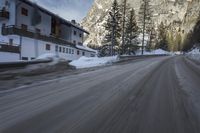 snow on the road and small buildings in the mountains side by side along a path with light poles