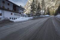snow on the road and small buildings in the mountains side by side along a path with light poles