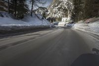 snow on the road and small buildings in the mountains side by side along a path with light poles