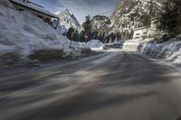 snow on the road and small buildings in the mountains side by side along a path with light poles