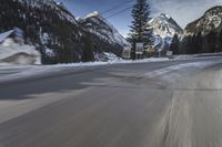 snow on the road and small buildings in the mountains side by side along a path with light poles