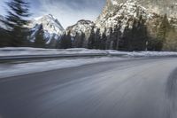 snow on the road and small buildings in the mountains side by side along a path with light poles