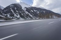a snow covered mountain is in the background while a car drives down the road in a blur