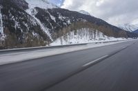 a snow covered mountain is in the background while a car drives down the road in a blur