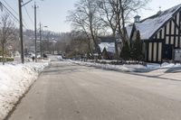 an empty street has many snow piles on the side and trees and power lines at each end