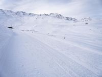 snow covered slope in the middle of a ski area as people ski on it near ski lift