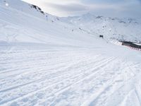 two people riding skis down a snow covered slope in the day time by a hill side