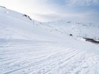 two people riding skis down a snow covered slope in the day time by a hill side