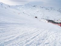 two people riding skis down a snow covered slope in the day time by a hill side