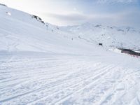 two people riding skis down a snow covered slope in the day time by a hill side