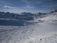 a group of people riding skis down a snow covered slope next to large mountains