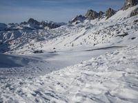 a group of people riding skis down a snow covered slope next to large mountains