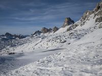 a group of people riding skis down a snow covered slope next to large mountains