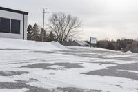 a parking meter is in the snow next to a building and an empty street in a country lane