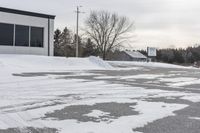 a parking meter is in the snow next to a building and an empty street in a country lane