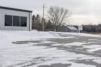 a parking meter is in the snow next to a building and an empty street in a country lane