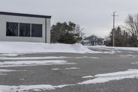 a parking meter is in the snow next to a building and an empty street in a country lane