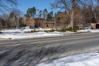 a street with snow on the ground next to a house and trees and a building