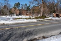 a street with snow on the ground next to a house and trees and a building