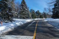 the snow covered road and street sign is empty of traffic with pine trees along it