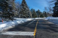 the snow covered road and street sign is empty of traffic with pine trees along it