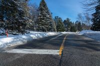 the snow covered road and street sign is empty of traffic with pine trees along it