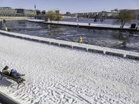 the view of a person sitting on a park bench covered in snow by a pool