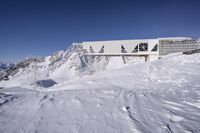 snow is covering the ground at the top of the mountain of a building with a walkway over it