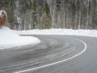 a very curvy road in the middle of the woods, covered with snow