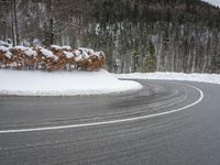 a very curvy road in the middle of the woods, covered with snow