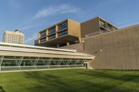 the grass is being mowed up and the building on the other side of it is taller than the building