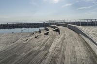 an empty wooden deck near water with steps, benches and railings along the side of it