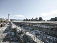 an area with rocks, stone, and a lighthouse near the sea shore in front of it