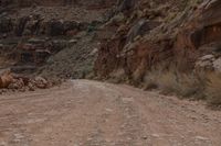 a woman is sitting on a motorcycle and waiting to cross the street on a dirt road in a canyon