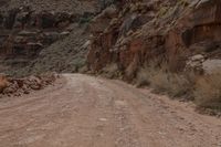 a woman is sitting on a motorcycle and waiting to cross the street on a dirt road in a canyon