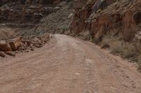 a woman is sitting on a motorcycle and waiting to cross the street on a dirt road in a canyon