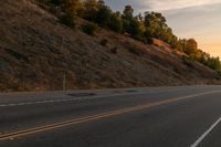 a woman is riding her bicycle down the road with the sunset behind her and hills