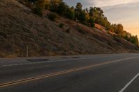 a woman is riding her bicycle down the road with the sunset behind her and hills