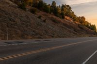 a woman is riding her bicycle down the road with the sunset behind her and hills