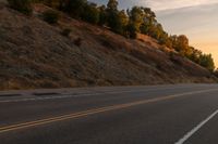 a woman is riding her bicycle down the road with the sunset behind her and hills