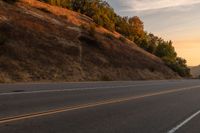 a woman is riding her bicycle down the road with the sunset behind her and hills